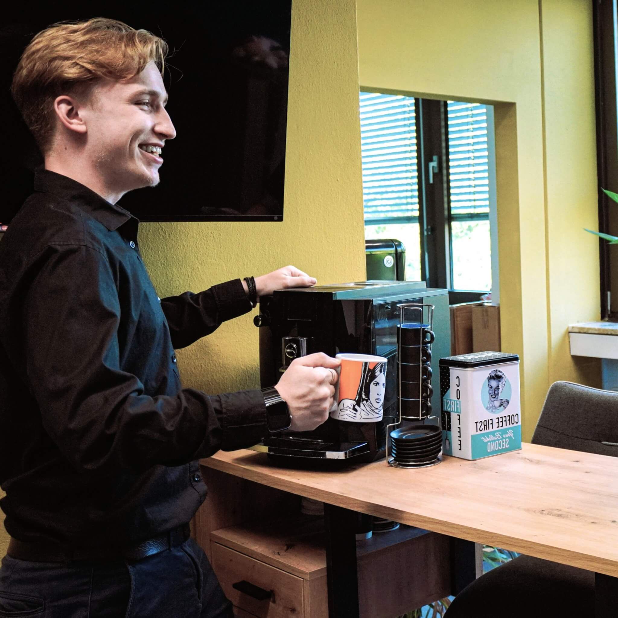 Karriere-Seite Bildmaterial: Joel, Mediengestalter bei taismo, lacht mit einer Star Wars Tasse in der Hand