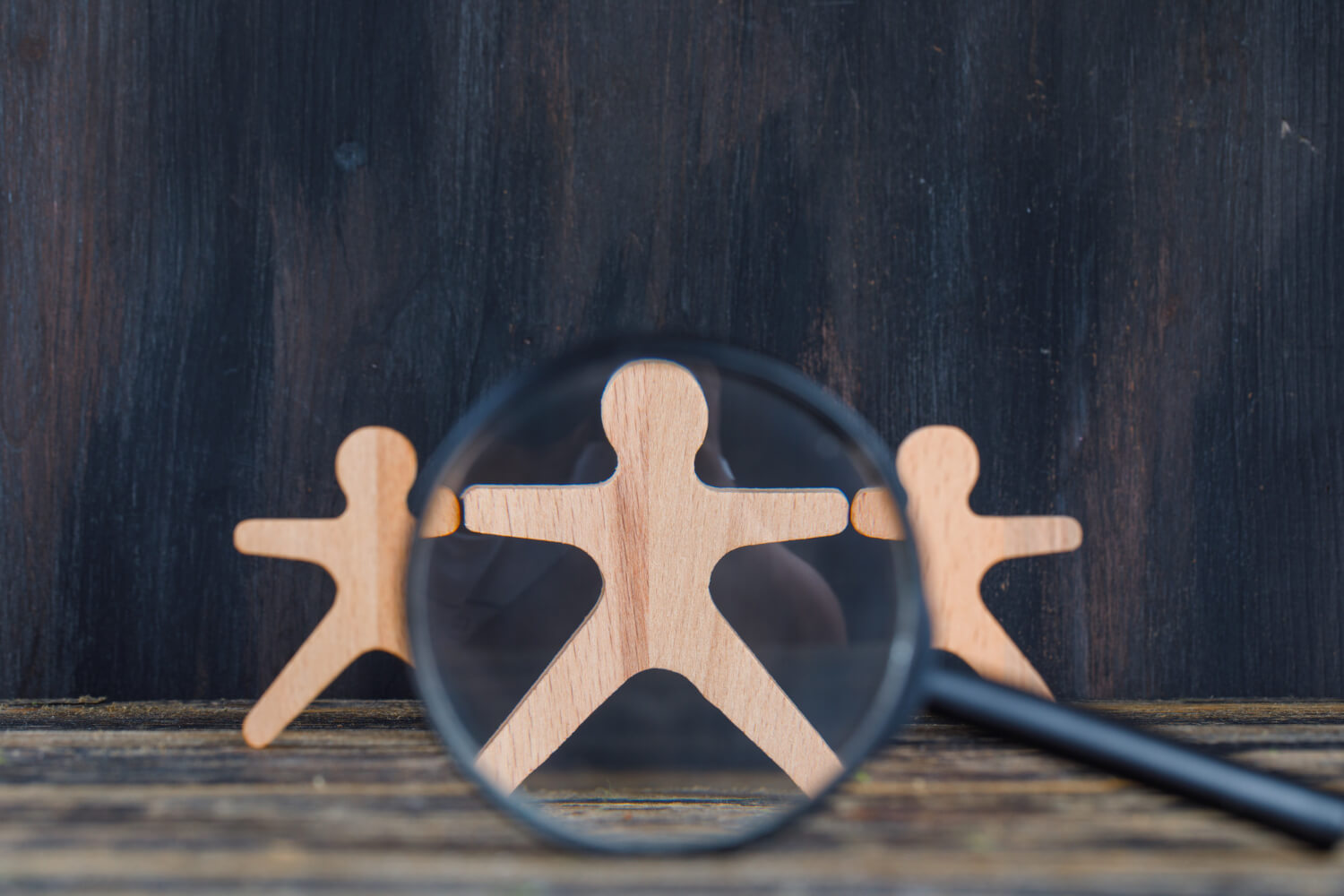 How to find employees: an employer searching for candidates among wooden figures under a magnifying glass